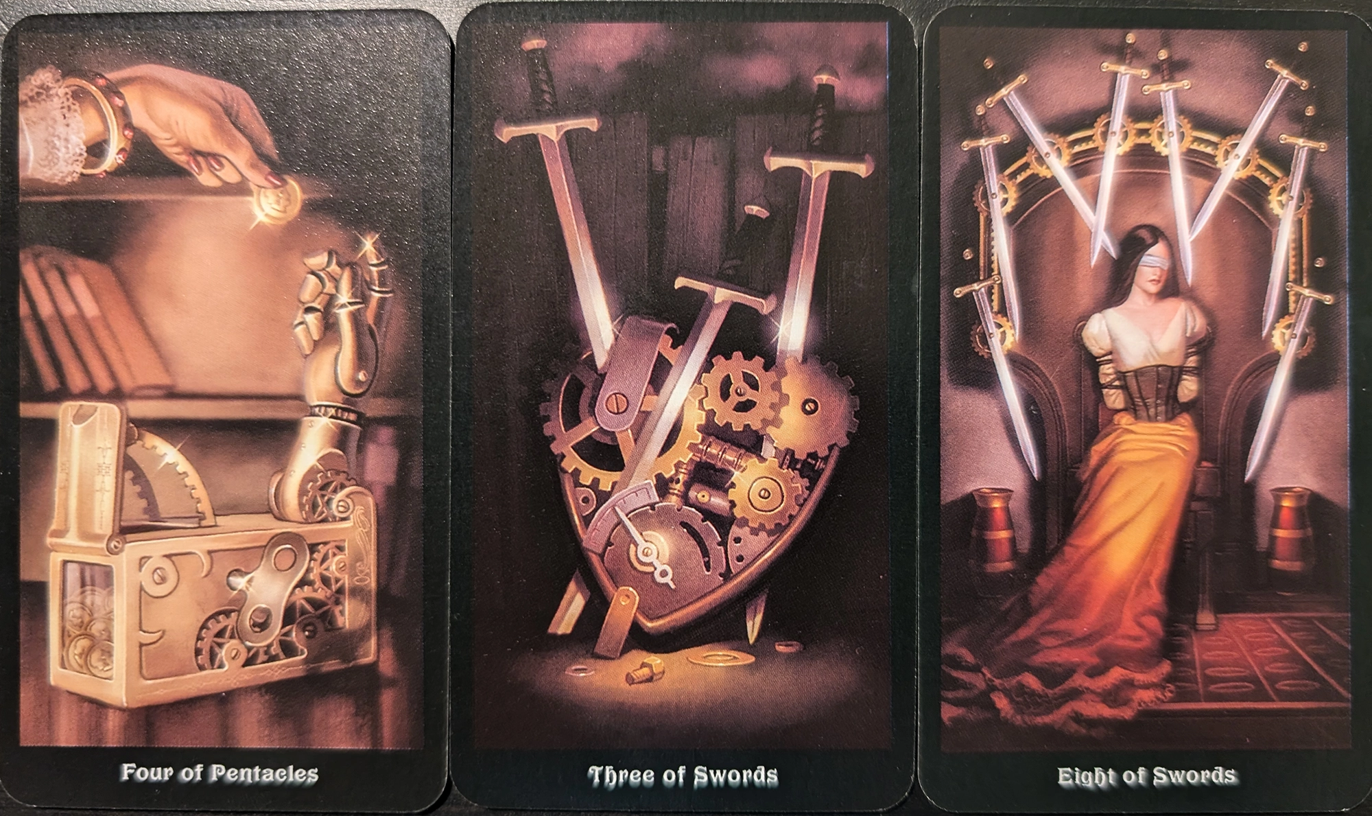 3 cards from the Steamounk Tarot deck of  the Four of Pentacles, Three of Swords, Eight of Swords. 