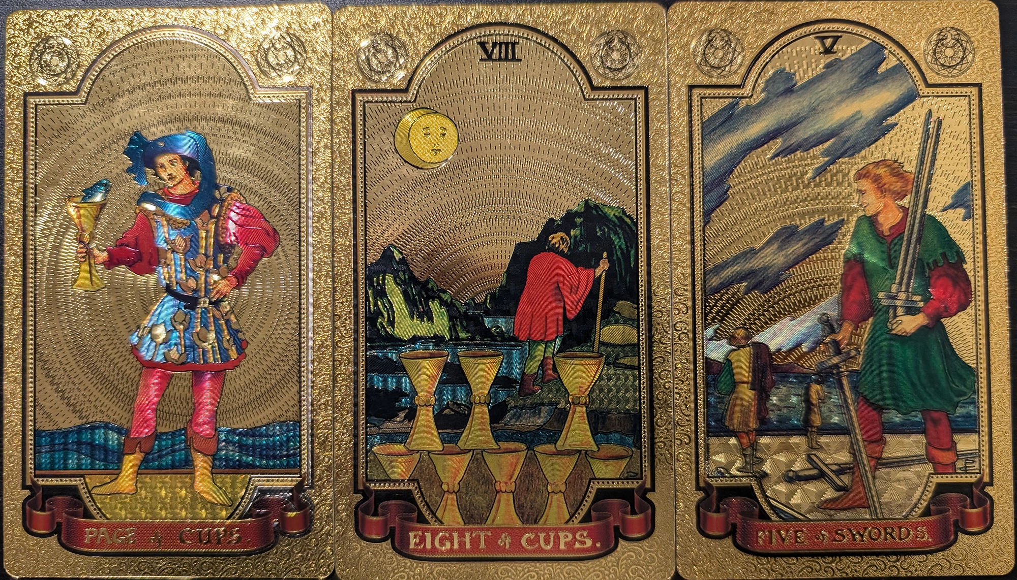 3 cards from the GoldFoil Tarot of Page of Cups, Eight of Cups, and the Five of Swords